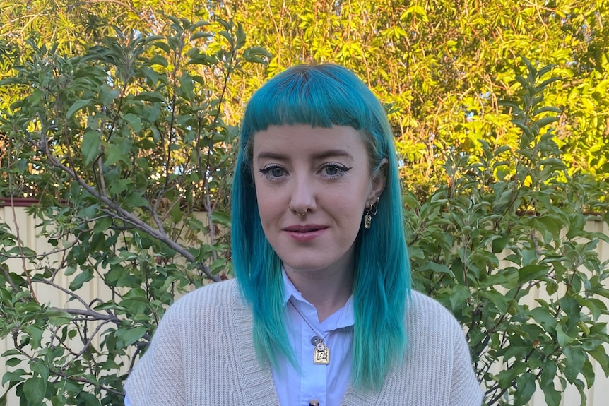 Madi - a young woman with blue-green hair, standing in front of a tree