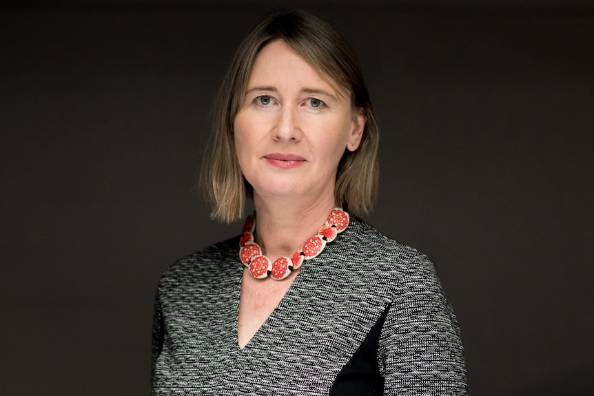 Rebecca Bentley - an older white woman in a gray dress and a gold necklace looks at the camera.